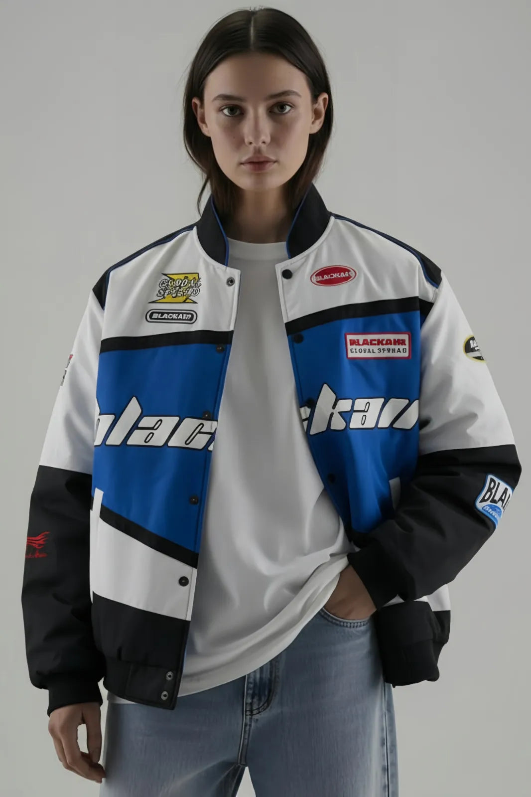 Female Model wearing a BalckAir Blue racing jacket with various logos on a gray background giving Front Pose
