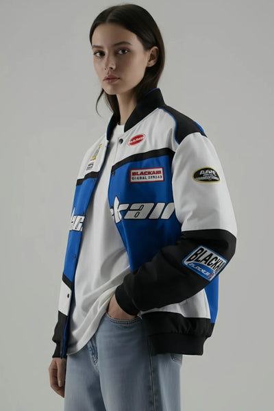 Female Model wearing a BalckAir Racing jacket with multiple brand logos on a gray background giving side pose