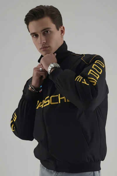 Man wearing a Porsche jacket with yellow text on a gray background giving side pose