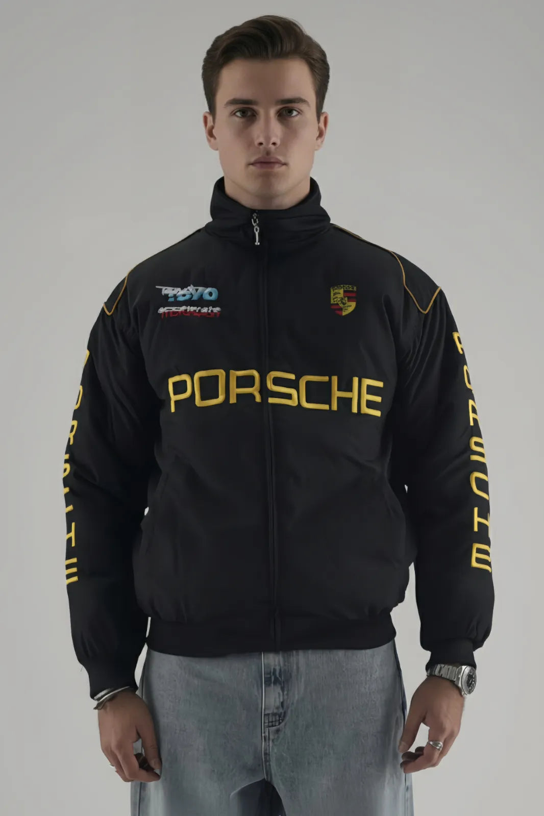 Person wearing a black Porsche jacket with logos on a gray giving background giving front pose