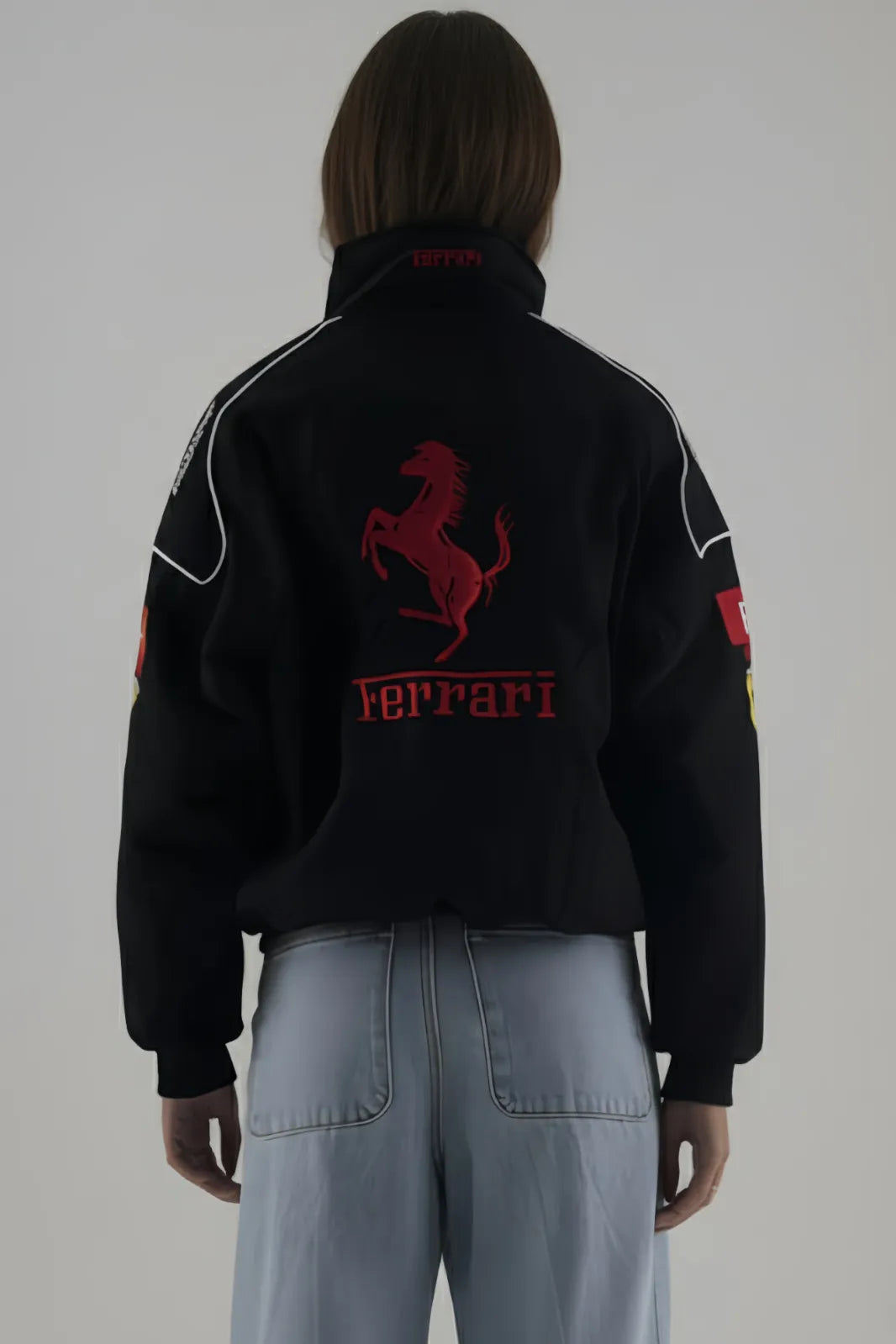 Person wearing a black Ferrari jacket and giving back pose with red logo on a plain background