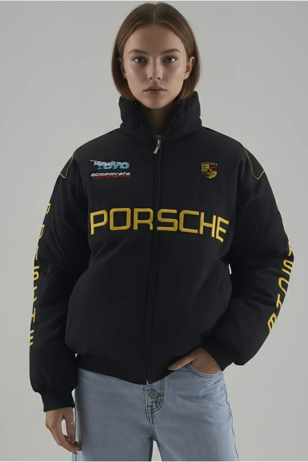 Female Model wearing a black Porsche hoodie with branding on a gray background giving front pose 