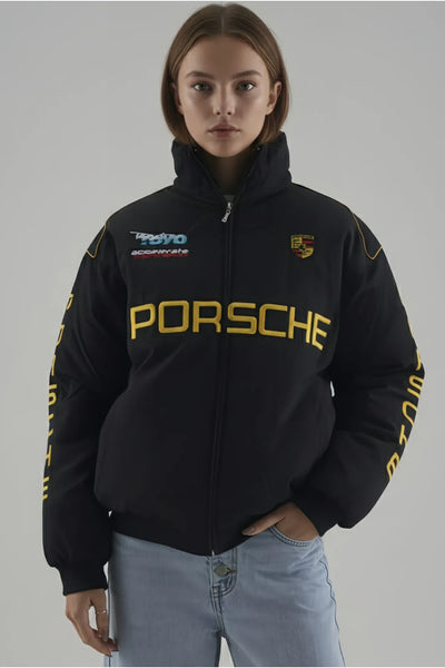 Female Model wearing a black Porsche hoodie with branding on a gray background giving front pose 
