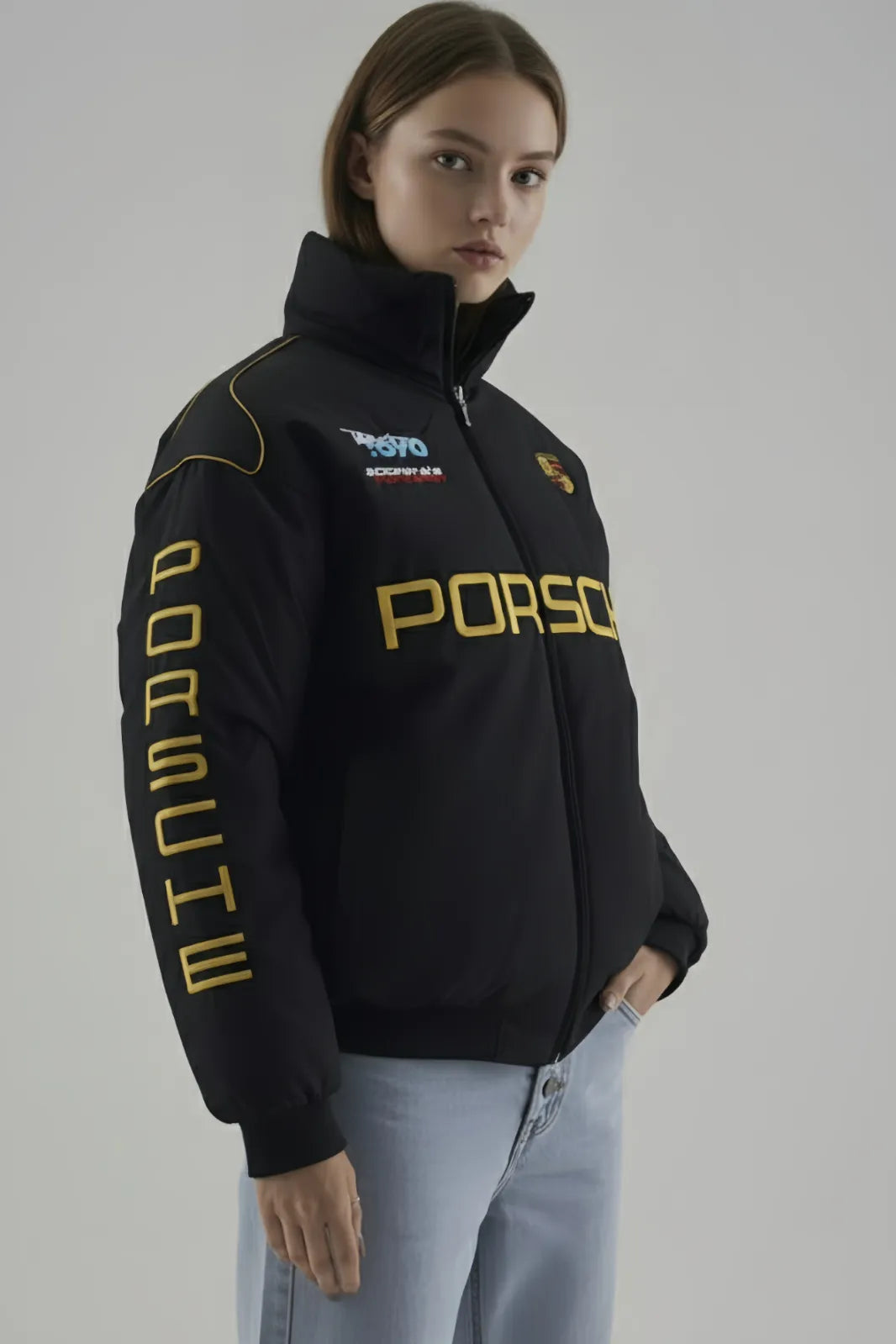 Person wearing a black Porsche jacket with yellow text on a gray background giving side pose