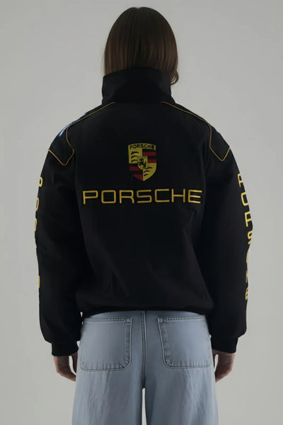 Female Model wearing a black Porsche jacket with logo and text on a plain background giving Back pose