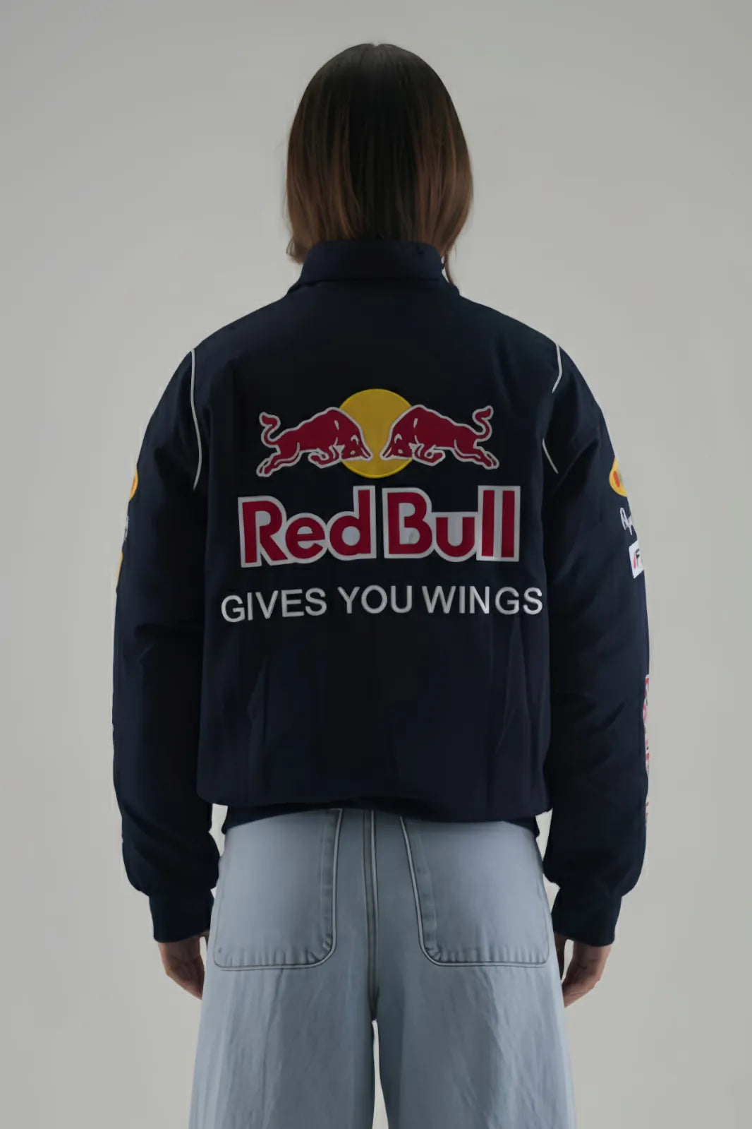 Female Model wearing a navy jacket with Red Bull logo and text on a plain background giving back pose