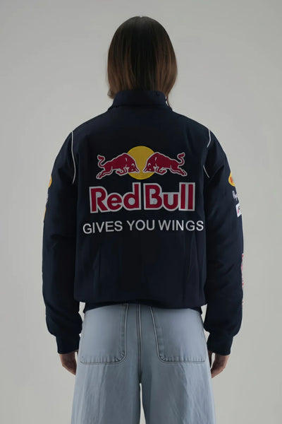 Female Model wearing a navy jacket with Red Bull logo and text on a plain background giving back pose
